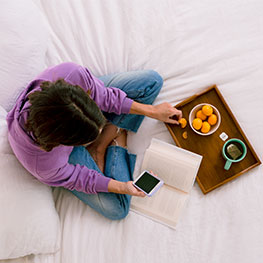send and receive money with zelle app image of woman sitting in bed with a book and tray of food and drink